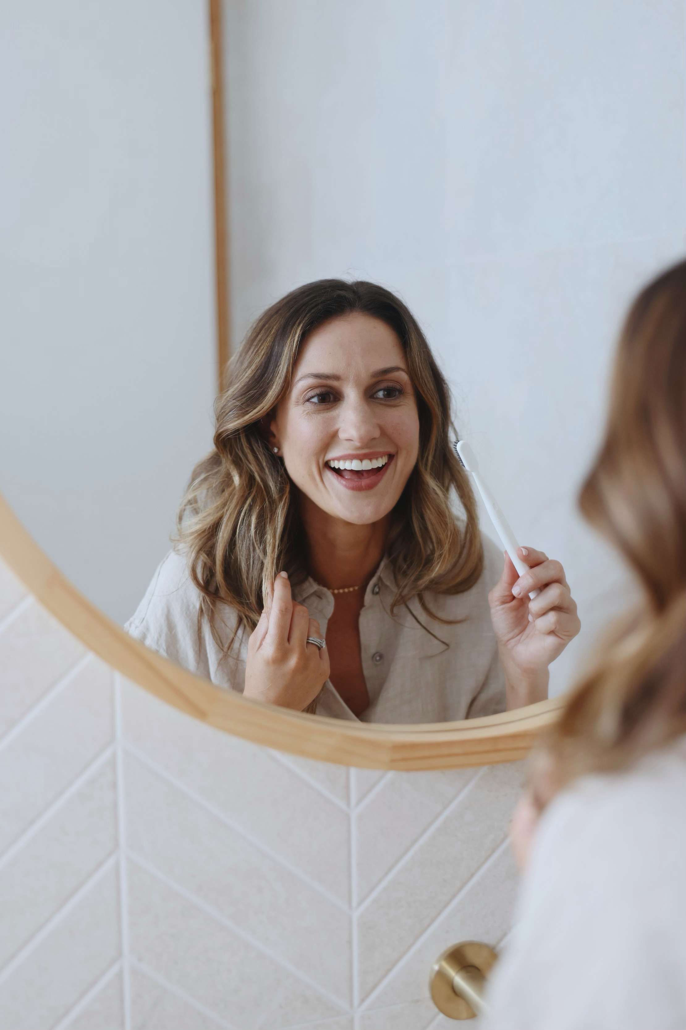 Woman smiling and brushing her hair in front of a mirror.