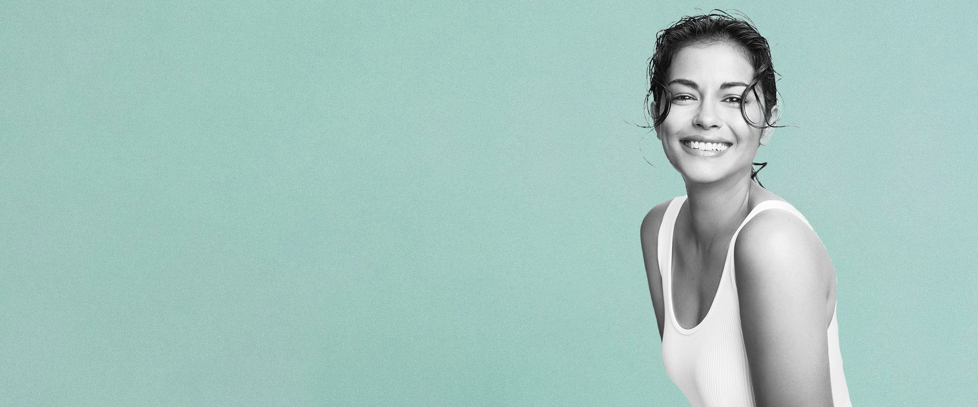 Woman in white tank top smiling against a light green background