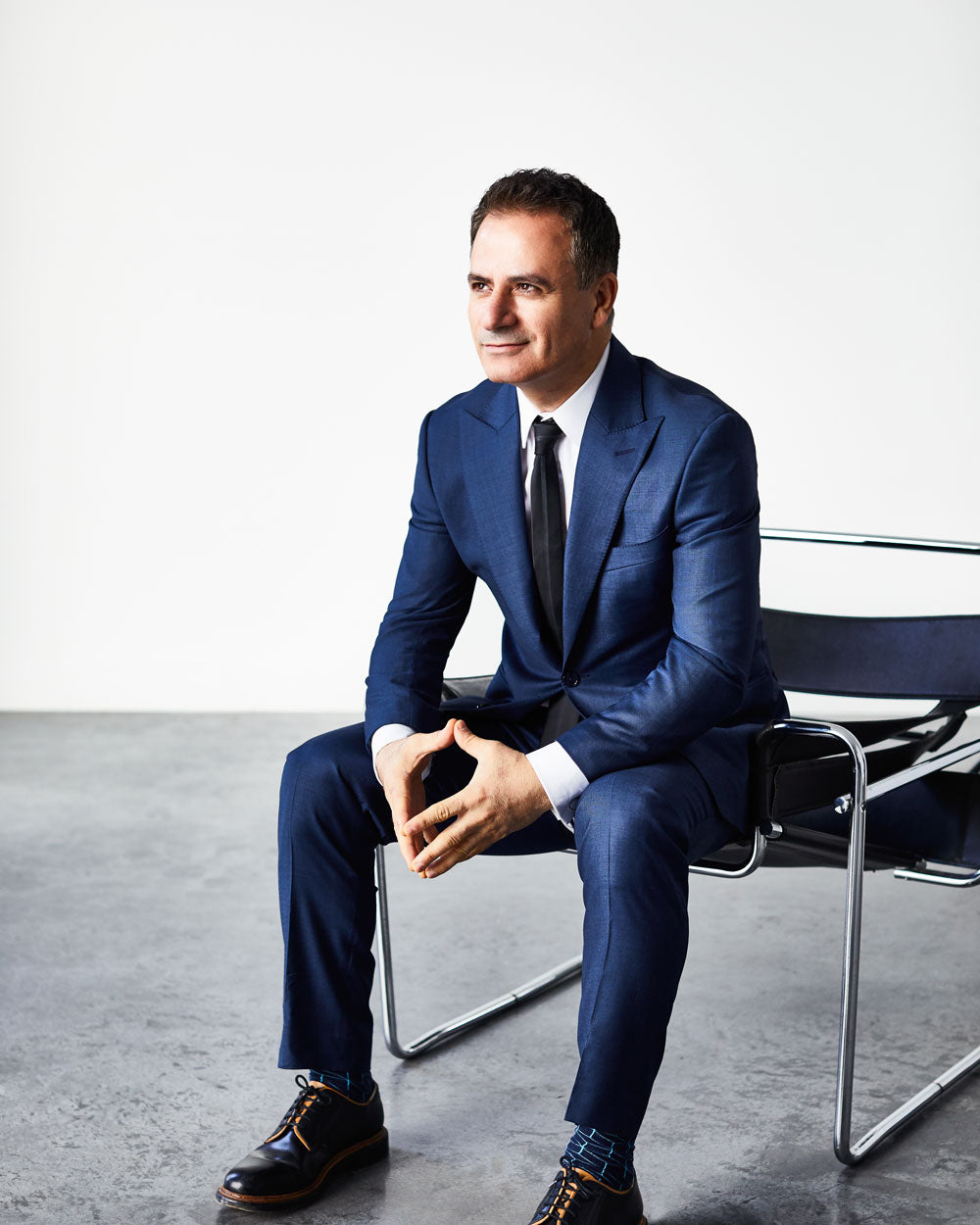 Man in a blue suit sitting on a chair in a minimalistic setting